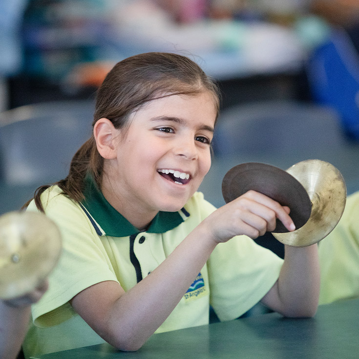 Student playing cymbals in the classroom at St Angela's Primary School Castle Hill