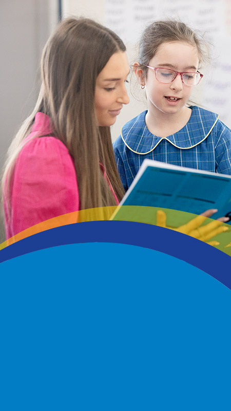 Teacher reading with her student in the classroom at St Angela's Primary School Castle Hill