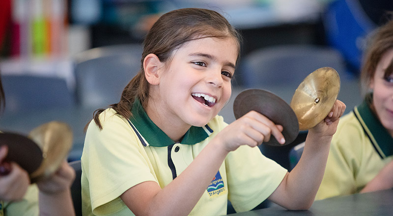 Student playing the cymbals in the classroom at St Angela's Primary School Castle Hill