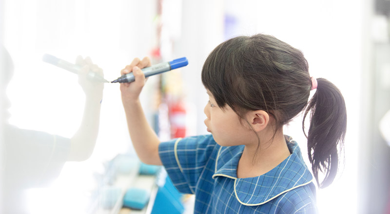 Student writing on a whiteboard in the classroom at St Angela's Primary School Castle Hill